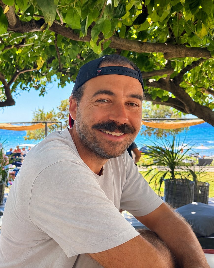 Dan Connolly smiling, sitting outdoors by the sea
